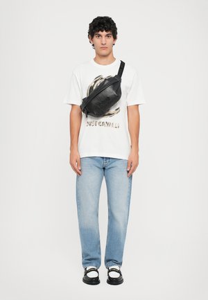 Zwarte lederen crossbody tas met een sleek ontwerp. Witte graphic t-shirt met dierenprint, blauwe jeans en zwarte schoenen met witte accenten.
