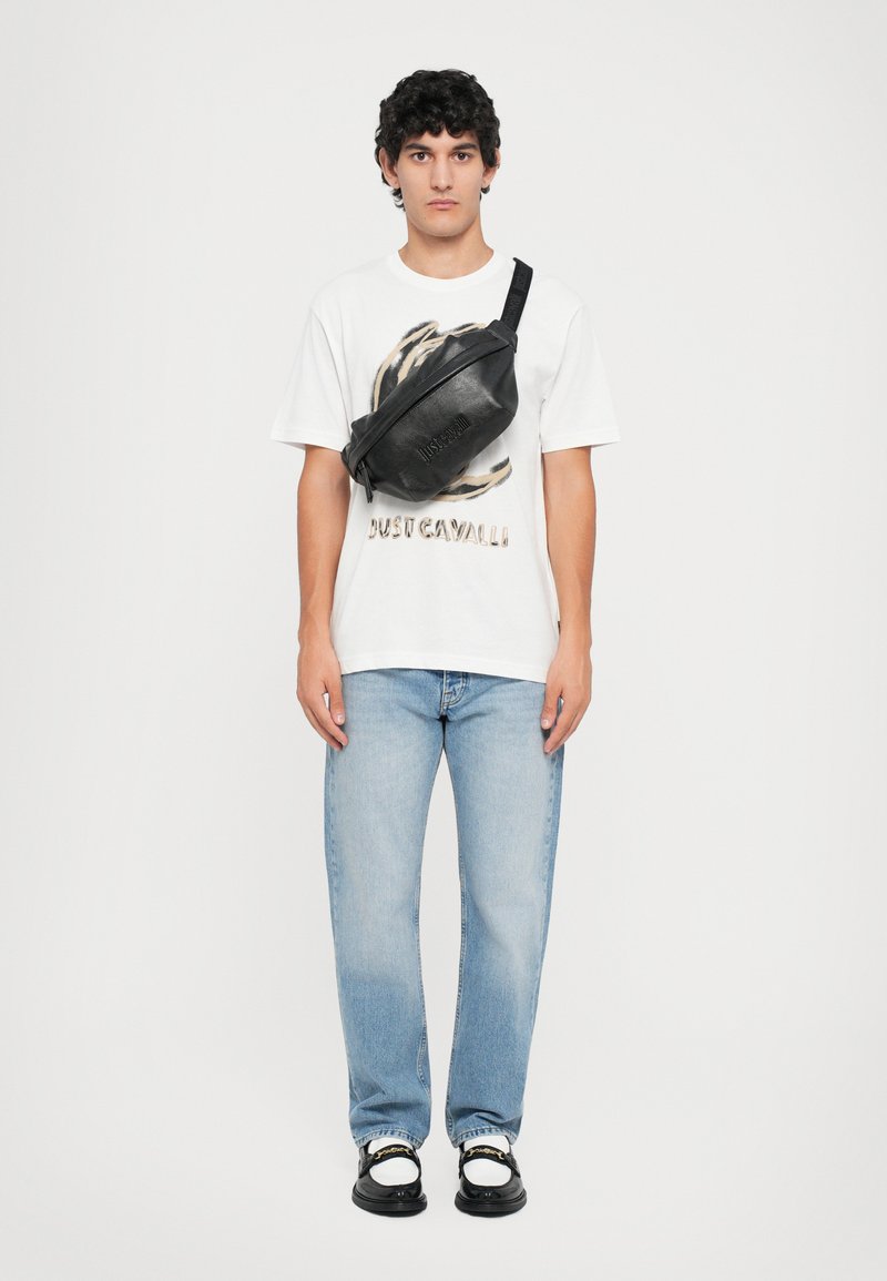 Borsa a tracolla in pelle nera dal design elegante. Maglietta grafica bianca con stampa animale, jeans blu e scarpe nere con dettagli bianchi.