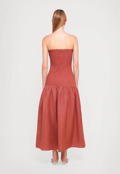 Strapless, rust-colored dress with a smocked bodice and ruffled top. Flowy, gathered skirt extends to the ankles. Smooth texture.