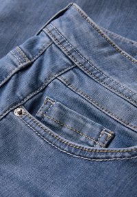 Jean en denim bleu avec une poche arrière dotée d'une fermeture à pression argentée, une couture distincte et une surface de tissu texturée.