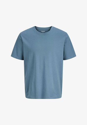 Tricou din bumbac bleu deschis cu mâneci scurte, asortat cu blugi largi de culoare verde deschis. Încălțămintea prezintă o combinație de culori alb și gri.