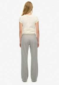 Un pantalon de survêtement gris clair avec une taille élastique, associé à un tee-shirt blanc ajusté, montré de dos sur un fond uni.