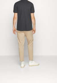 T-shirt à manches courtes gris charbon, pantalon beige droit, et baskets blanches. Design épuré avec une texture douce et une palette de couleurs neutres.