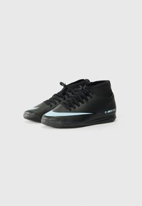 Chaussures de soccer noires avec un design basse, dotées d'un swoosh bleu clair, de lacets et d'une semelle en caoutchouc texturé pour une meilleure adhérence.