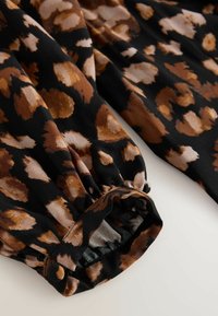 Tkanina s uzorkom leoparda na crnoj podlozi s smeškim i krem točkicama. Ima detalje s elastičnim manžetama, mekanu teksturu i glatku draperiju.
