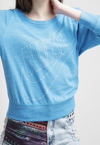 Blå heather-tröja med rundad halsringning och långa raglanärmar. Har en stor vit Nike-logotyp tryckt på framsidan.