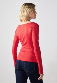 Punane ribadega pika varrukaga ülemise osa, laia kaelusega, istuv disain ja tekstuurne kangas. Koos tumedate siniste teksadega.
