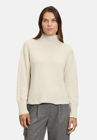 Pull à col roulé beige clair avec des poignets et un ourlet côtelés, confectionné dans un matériau doux, présentant une coupe décontractée et une surface texturée.