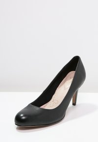 Chaussure à talon haut en cuir noir avec un bout rond et un talon fin. Texture lisse avec un léger éclat. Design minimal et sans embellissements visibles.