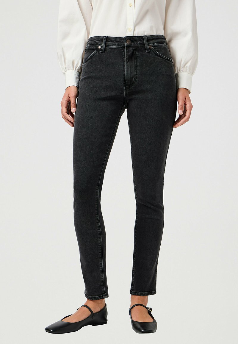 Mismas jeans negros ajustados con un corte slim, hechos de denim, presentan un estilo de cinco bolsillos y una cinturilla clásica. Combinados con zapatos planos negros.