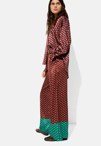 Długi, luźny strój o bordowej podstawie, w kropki i turkusowych mankietach. Wykonany z gładkiego materiału. Brązowe obuwie.