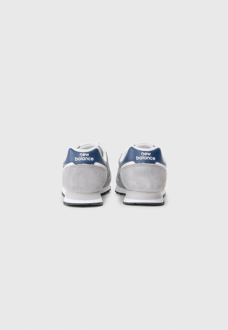 Baskets en suède gris avec un accent de talon bleu marine, empeigne en maille blanche et semelle en caoutchouc noir. Présente un logo "new balance" à l'arrière.