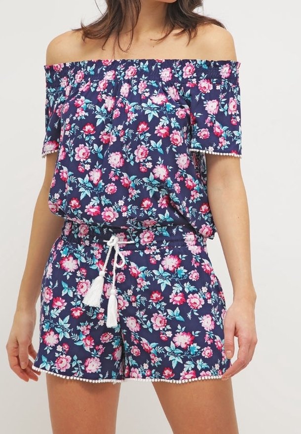 Jumpsuit floreale blu scuro off-the-shoulder, caratterizzato da fiori rosa e turchesi, banda elastica e dettagli con frange in vita e all'orlo.