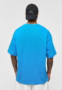 Blauwe katoenen T-shirt met een relaxed fit en korte mouwen, voorzien van een eenvoudige ronde hals. Zwarte pet met geborduurde tekst op de achterkant.