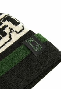 Black and green knit beanie featuring a textured pattern and a woven label with a graphic design. The color scheme includes cream accents.