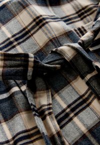 Kariertes Gewebe in Grau, Beige und Marineblau mit einer weichen, strukturierten Oberfläche. Es zeigt sich durchkreuzende Linien unterschiedlicher Breite, die ein kariertes Muster bilden.