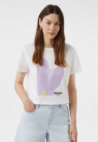 Biała koszulka z bawełny z purpurową grafiką kwiatową i napisem "lawenda la fleur", w zestawieniu z jasnoniebieskimi dżinsami.