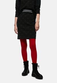 Schwarzer Rock mit Sternenmuster, weißen Akzenten, kombiniert mit roten Leggings und schwarzen Schnürstiefeln. Glattes Material mit strukturiertem Design.