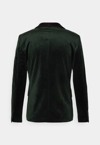 Giacca in velluto verde scuro con colletto nero, spacchetto singolo sul retro e dettagli con bottoni sui polsini. Tessuto liscio, vestibilità su misura.