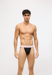 Čierny tanga s mäkkým, svetloružovým pásom Calvin Klein. Tkanina vyzerá hladko a obopína telo, navrhnutá pre pohodlie a podporu.