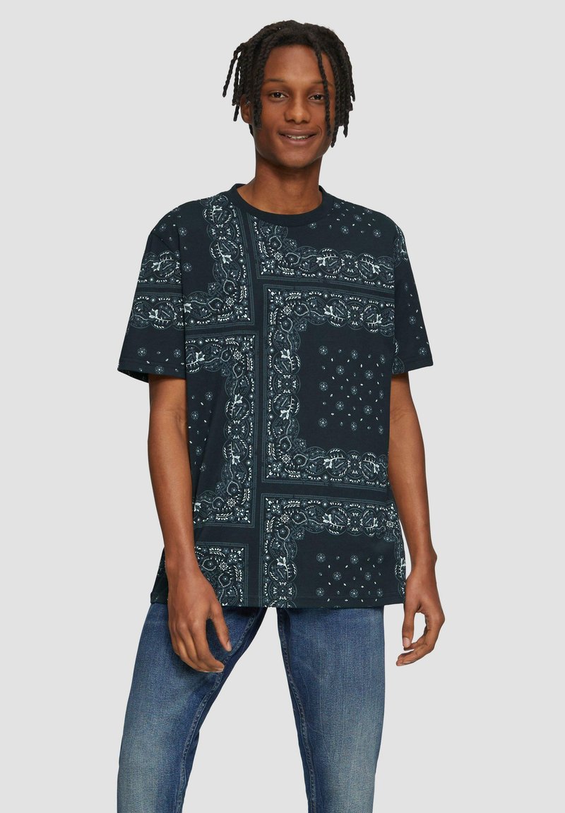 Zwarte t-shirt met witte bandana print, met ingewikkelde patronen en accenten. Losse pasvorm met korte mouwen en een ronde halslijn.