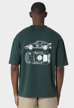 Homme portant un t-shirt vert foncé avec des illustrations blanches d'une voiture de sport vintage vues de côté et de dessus dans le dos.