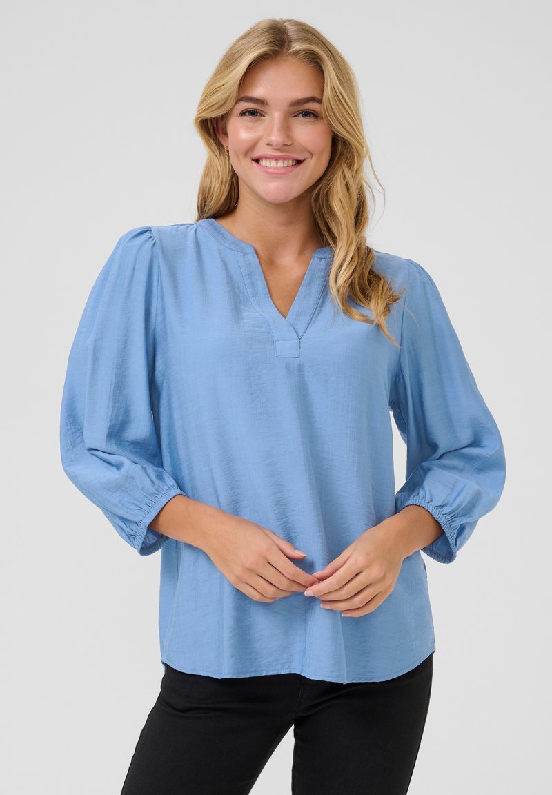 Lichtblauwe blouse met een V-halslijn, driekwart pofmouwen en een relaxte pasvorm. Gestructureerde stof met een subtiele glans, bijpassende zoom.