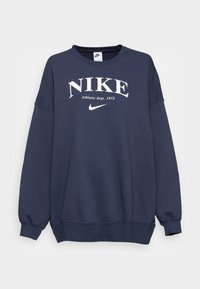Marineblå sweatshirt med rund halsringning, stor vit "NIKE"-logotyp, text f ör idrottsavdelning och ribbade muddar och nederkant. Mjuk tygtextur.