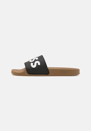 Sandale slide marron avec une sangle noire comportant de grandes lettres blanches "SS" et le nom de la marque "BOSS" embossés sur le côté de la semelle.