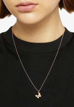 Close-up of person wearing a gold chain necklace with a small butterfly pendant over a black crew-neck shirt.