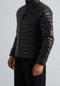 Veste matelassée noire avec un design matelassé, un col montant et une fermeture éclair. Texture douce avec des panneaux latéraux mats contrastants.