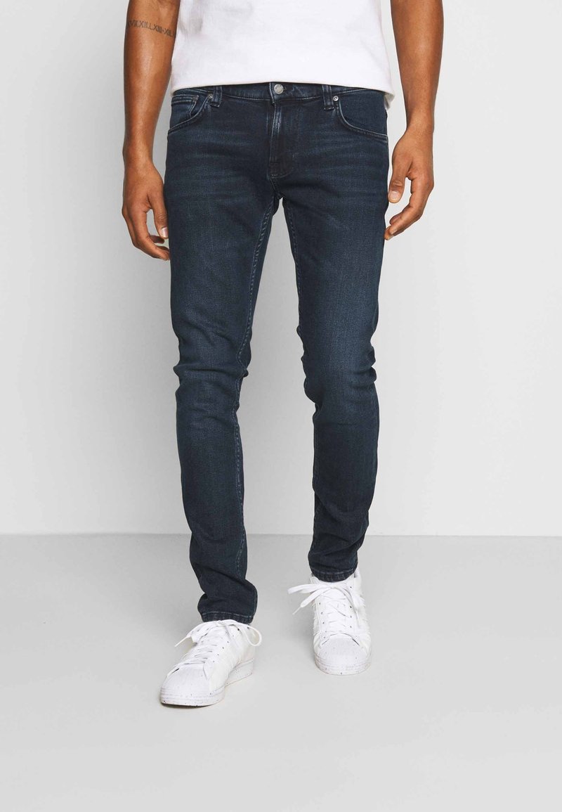 Mörkblå denimjeans med slim fit, som har fem fickor, dragkedja och diskret blekning. Stylingen kompletteras med vita sneakers.