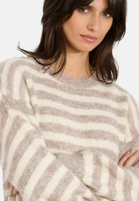 Maglione a righe in morbido filato beige e crema. Vestibilità ampia con maniche larghe. Tessuto testurizzato con strisce orizzontali di larghezze variabili.