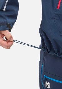 Granatowa wodoodporna kurtka z regulowanym sznurkiem w talii i niebieskimi zamkami. Materiał jest lekki i teksturowany.