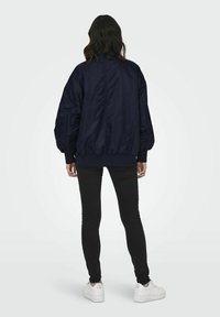 Námořnická bombarďácká bunda s elastickými manžetami a lemem, s hladkou texturou. V kombinaci s černými skinny džíny a bílými teniskami.