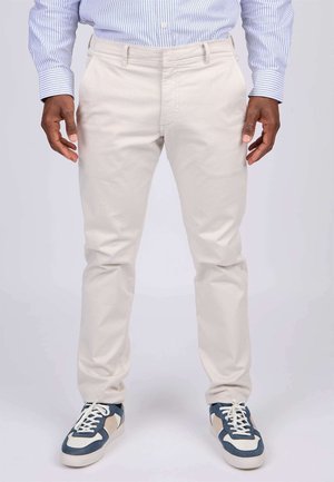 Chinos beige clair à coupe droite, dotés de poches avant et d'une texture lisse, associés à des baskets navy et blanches.