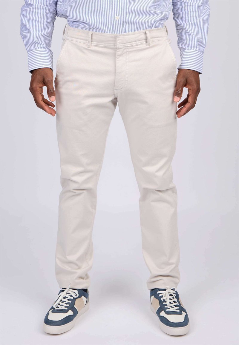 Chinos beige clair à coupe droite, dotés de poches avant et d'une texture lisse, associés à des baskets navy et blanches.
