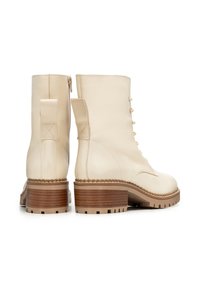 Stivaletti in pelle beige con tacco alto e texturizzato, punta tonda, chiusura con lacci e dettaglio di rinforzo sul tallone.
