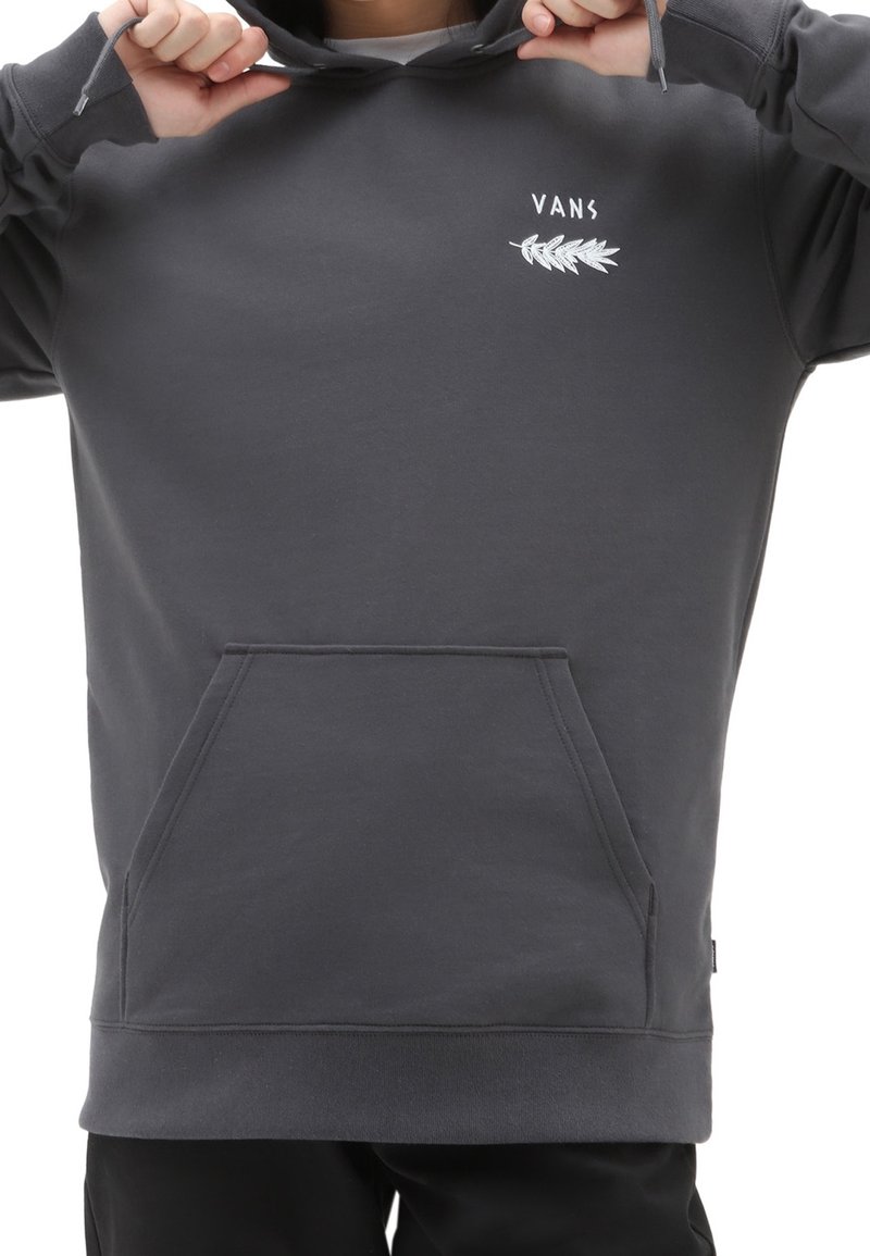 Personne portant un sweat à capuche Vans gris foncé avec un logo feuille blanche sur la poitrine, tenant les cordons de la capuche avec les deux mains.