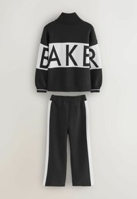 Suéter de punto en blanco y negro con el texto "BAKER", cuello alto y mangas anchas. Combinado con pantalones negros con franjas blancas a los lados.