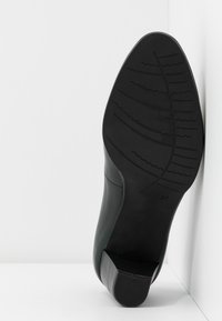 Black sole of a heeled shoe with patterned tread, size 37, positioned upright against a white cornered background.