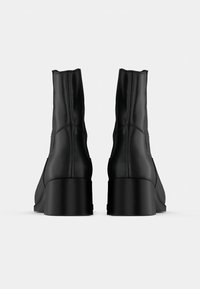 Černé kožené kotníkové boty s zakřiveným podpatkem, s elegantním designem, hladkou texturou a viditelnými švovými detaily po stranách.