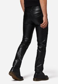 Zwarte leren broek met een slim fit, met een gladde textuur en veterdetails langs de zijkanten. Draagt samen met veterlaarzen.