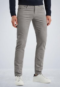 Jeans de algodón gris claro con un corte ajustado, diseño de cinco bolsillos y sutiles detalles de costura. Combinados con zapatillas blancas con acentos en negro.