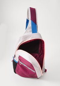 Mochila sling com tecido branco, bordô e preto, com uma alça azul, um bolso principal e um bolso frontal com fecho éclair e detalhes em rosa.