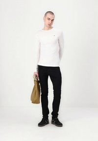 Valge pika varrukaga särk, mustad kitsad püksid, mustad tossud, käes pruun käekott. Lihtne disain ilma nähtavate mustrite või aksentiideta.