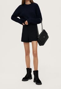 Jersey de punto de marina, pantalones cortos ajustados negros, bolso de mano negro acolchado con correa de cadena y botas de tobillo negras con cordones y suela gruesa.