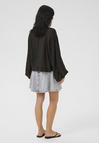 Schwarzes leichtes Oberteil mit weiten Ärmeln und cropped Länge, kombiniert mit einem hellgrauen Jeansrock. Glatte Textur, einfaches Design.