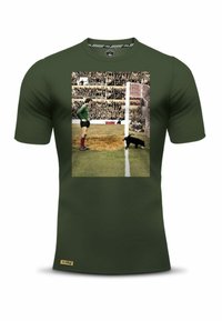 Olijfgroene t-shirt met een vintage print van een doelman en een hond, met een gestructureerde grafische afbeelding tegen een stadionachtergrond.
