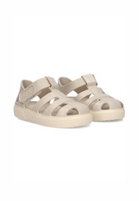 Beige plastic sandals with cut-out design and adjustable strap. Textured sole for grip. Iconic logo on the side. Lightweight and breathable.